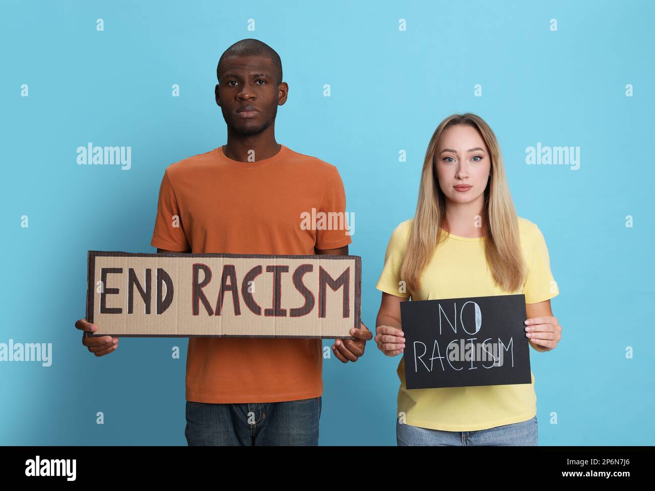Une jeune femme et un Africain américain tenant des signes avec l'expression mettre fin au racisme sur fond bleu clair Banque D'Images