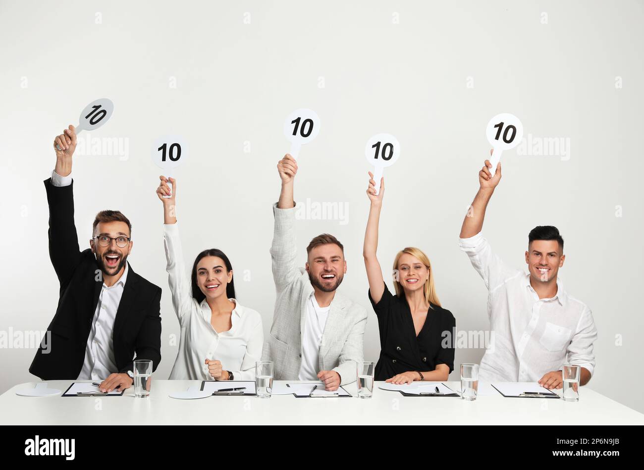 Panel de juges portant des affiches avec le score le plus élevé à la table sur fond blanc Banque D'Images
