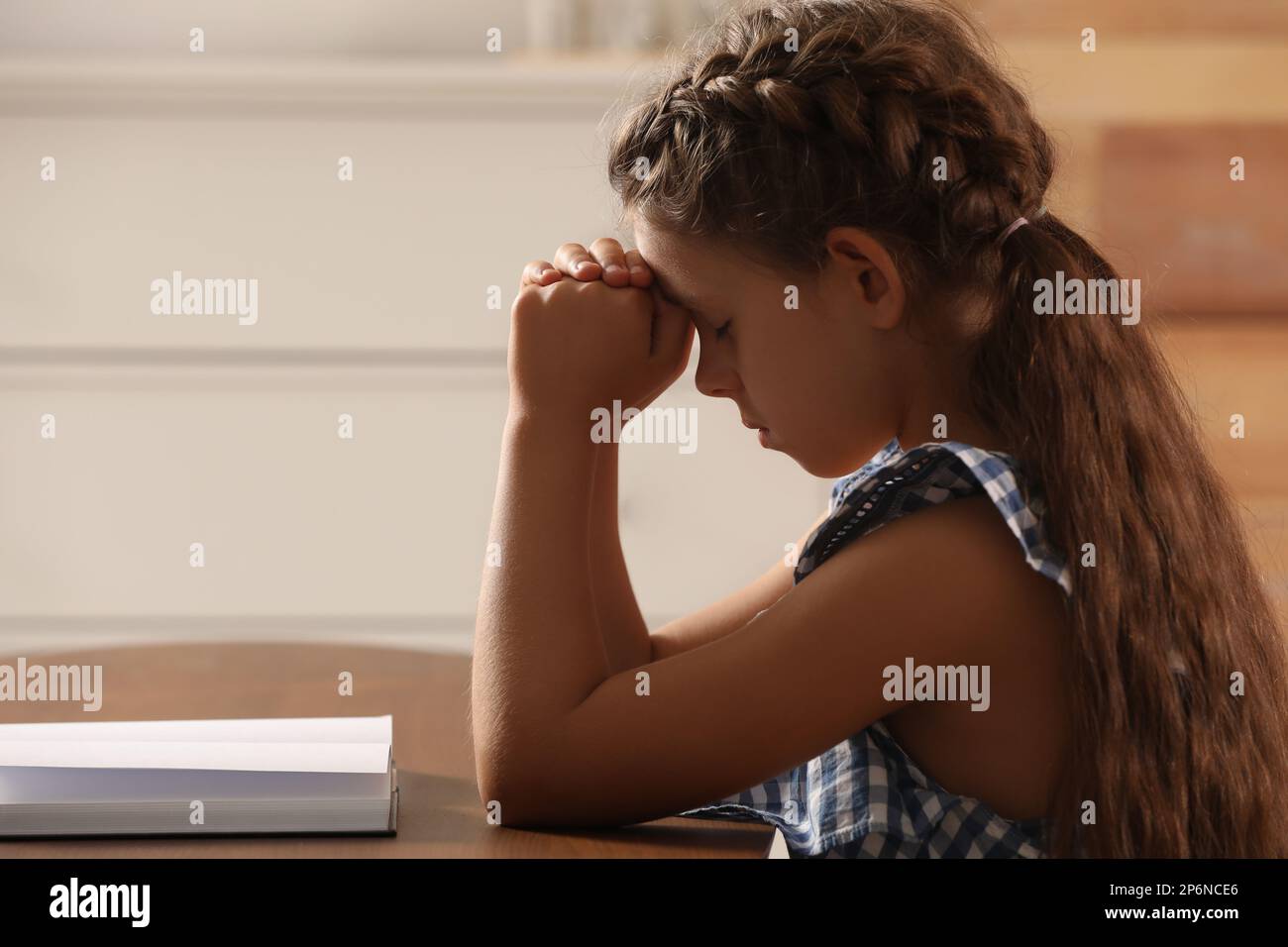 Petite fille mignonne priant sur la Bible à table dans la chambre Banque D'Images