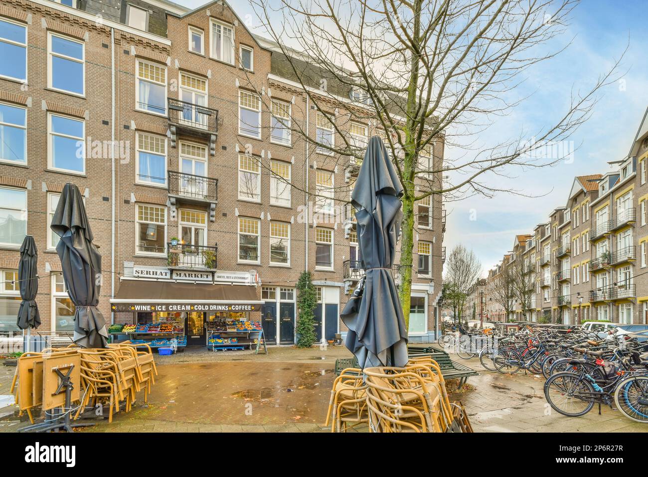 Amsterdam, pays-Bas - 10 avril 2021 : quelques tables et chaises avec parasols au sol devant une rangée de vélos garés devant un immeuble Banque D'Images