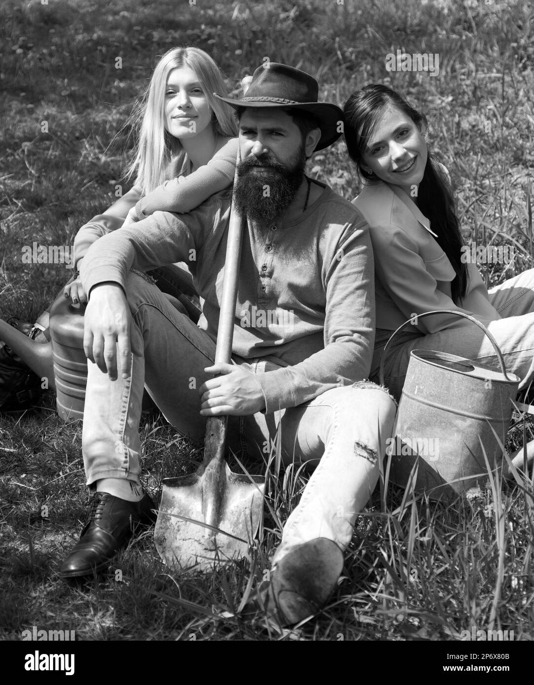 Amis assis sur l'herbe au jardin de printemps.Portrait d'un fermier de race blanche avec une pelle et une fille de deux amis.Détente après un travail acharné. Banque D'Images