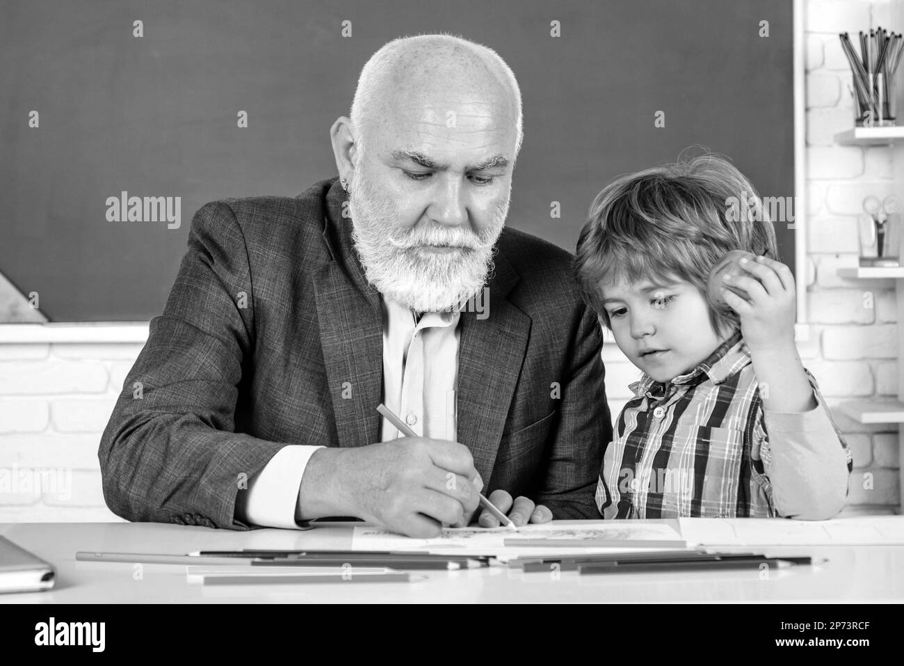 Happy son et grand-père assis à un bureau à l'intérieur. Journée mondiale des enseignants. Concept de génération et de relations familiales. Banque D'Images