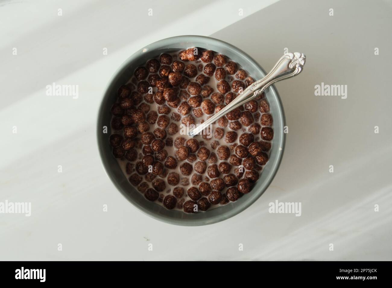 Les céréales et le lait du petit déjeuner sont dans un bol vert avec une cuillère en métal sur une table blanche. Les céréales sont prêtes à manger. Vue de dessus d'un petit déjeuner de céréales. Banque D'Images
