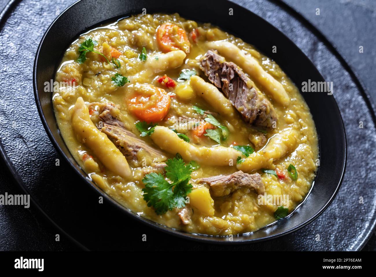 gros plan de petits pois, soupe de petits pois avec boulettes, légumes et bœuf dans un bol noir sur table en béton, cuisine jamaïcaine Banque D'Images