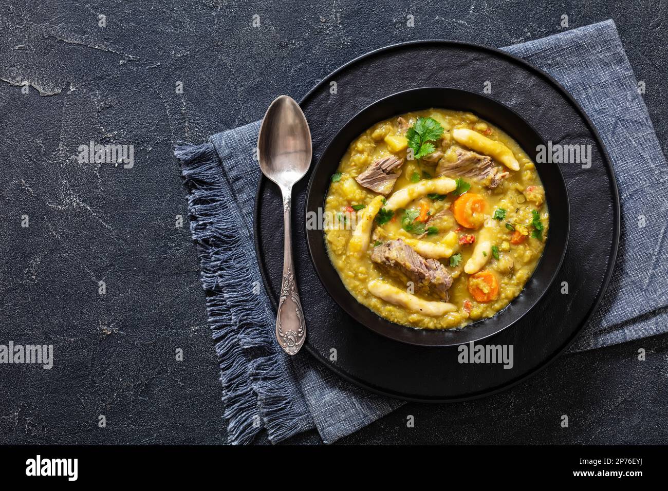 petits pois, soupe de petits pois avec boulettes et bœuf dans un bol noir sur table en béton avec cuillère, cuisine jamaïcaine, vue horizontale d'en haut, plat la Banque D'Images