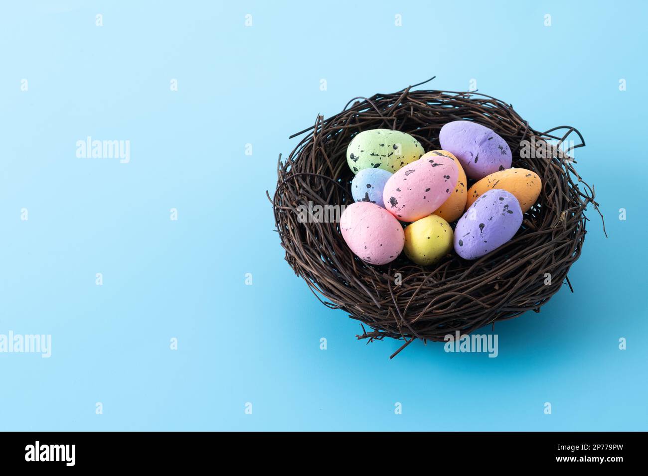 Œufs de Pâques colorés à l'intérieur d'un nid sur fond bleu Banque D'Images