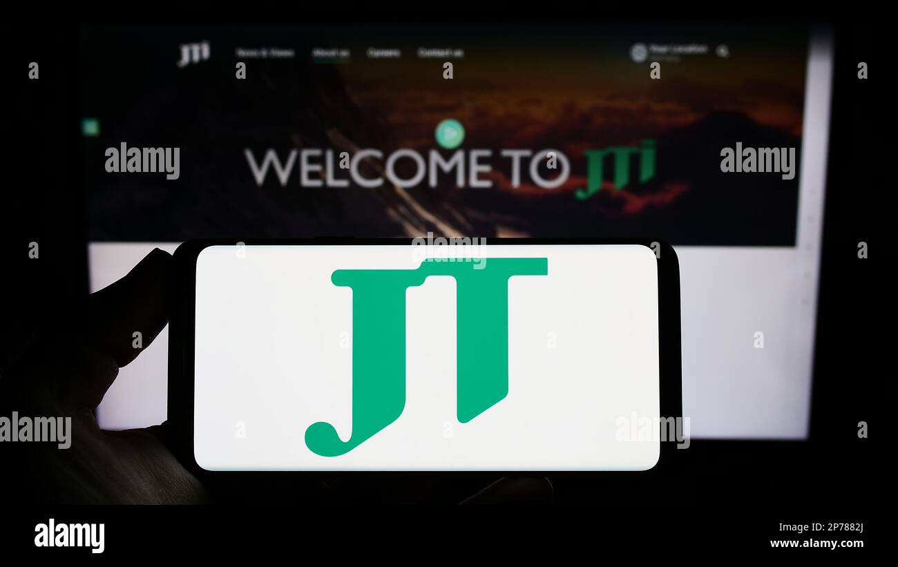 Personne tenant un smartphone avec le logo de la société de cigarettes Japan Tobacco Inc (JT) à l'écran en face du site Web. Mise au point sur l'affichage du téléphone. Banque D'Images