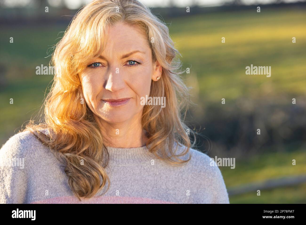 Belle femme d'âge moyen attentionnés à l'extérieur souriant au soleil de l'heure d'or Banque D'Images