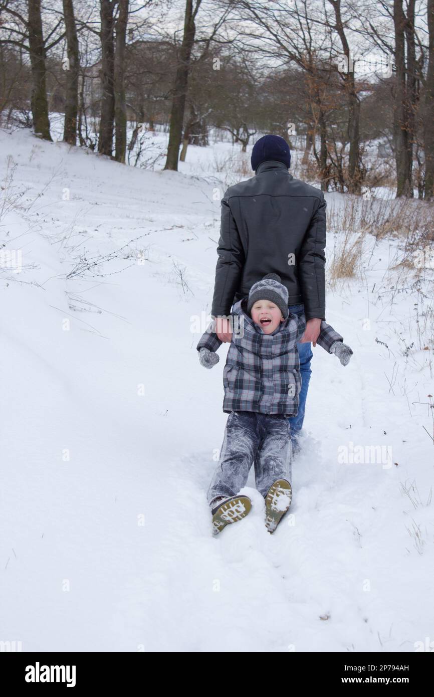 les frères plus âgés tirent leurs mains sur la neige de leur jeune frère à la maison Banque D'Images