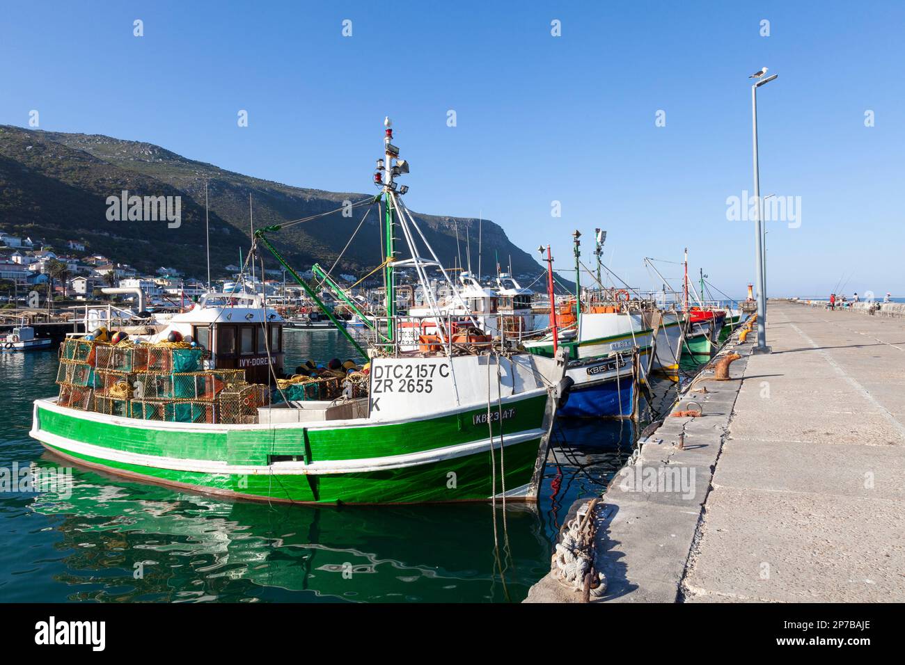 Bateaux de pêche amarrés dans le port de Kalk Bay, le Cap, le Cap occidental, Afrique du Sud au coucher du soleil, vue le long du quai avec pêcheur à distance Banque D'Images