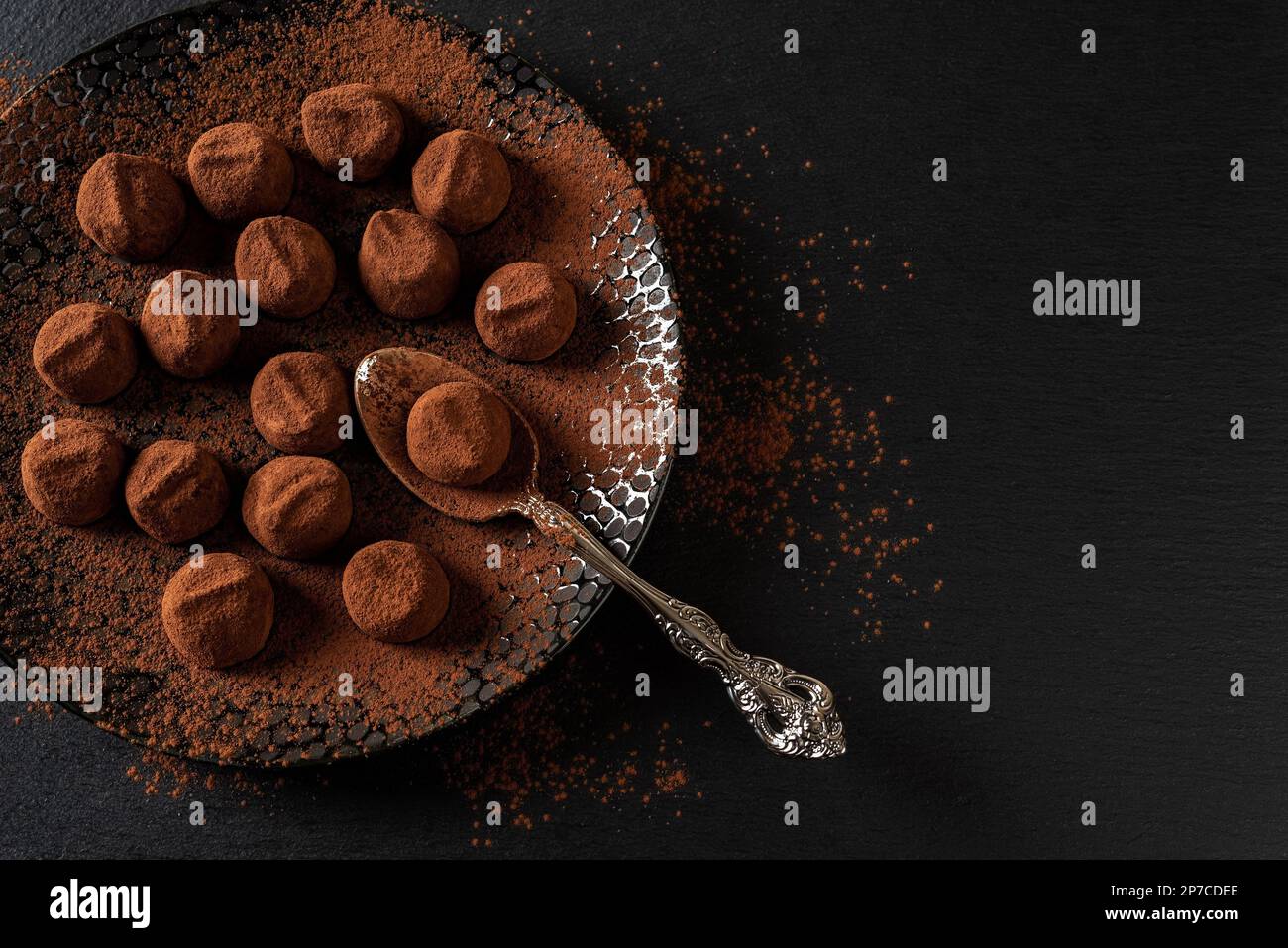 Boulettes de truffe de chocolat et cuillère sur une assiette noire. Bonbons au chocolat noir faits maison parsemés de poudre de cacao. Concept de nourriture douce. Copier l'espace. Banque D'Images