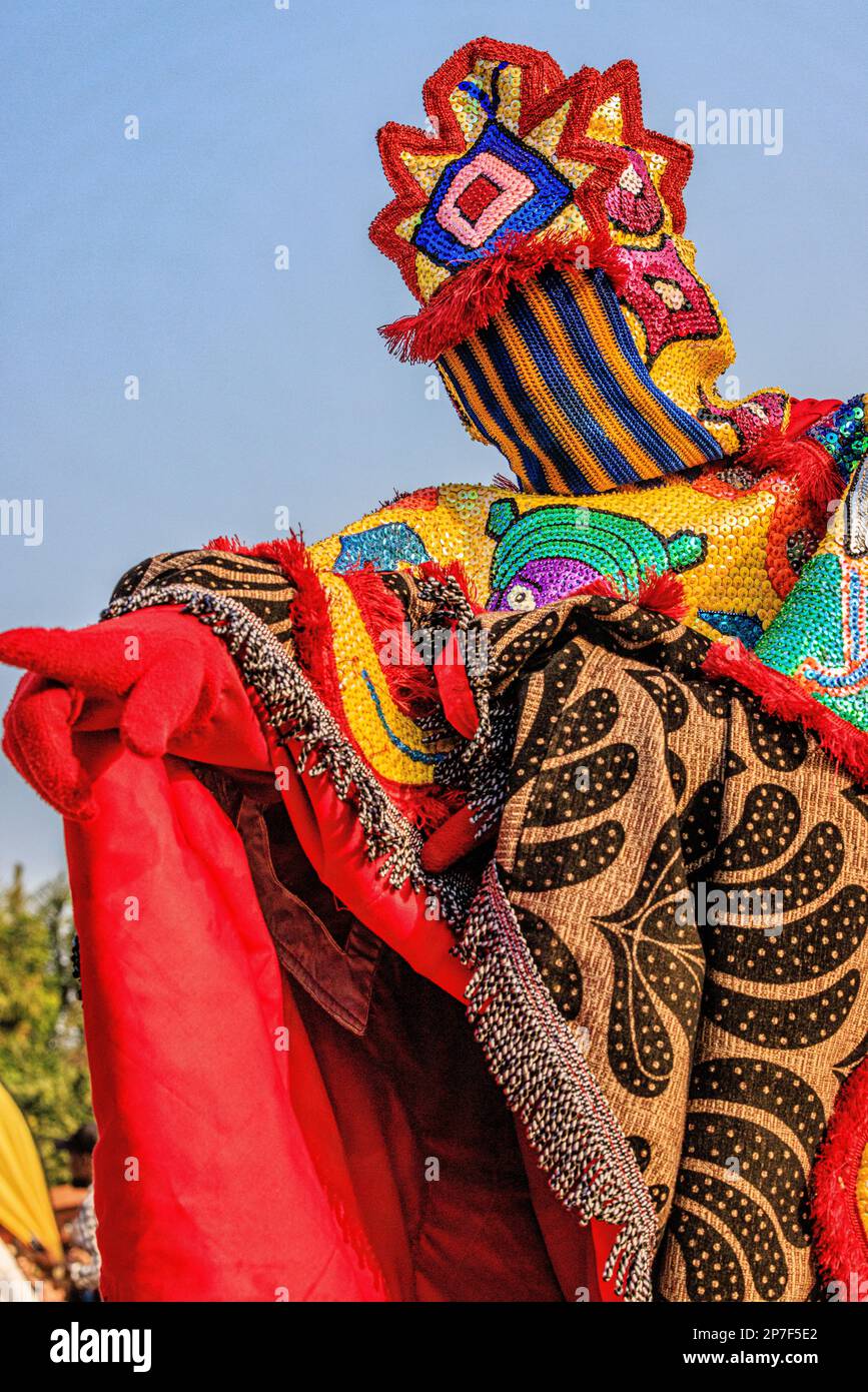 l'eguinguin aux couleurs vives avec masque à rayures pointe une main gantée rouge vers l'extérieur lors du festival voodoo annuel de ouidah au bénin Banque D'Images