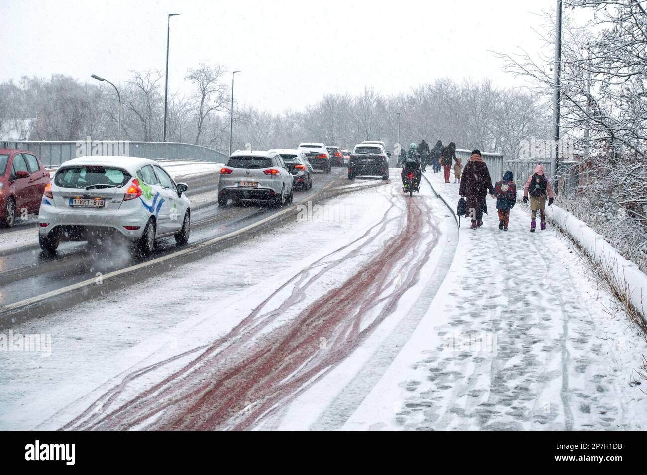 Voitures et enfants marchant vers l'école sur une chaussée glissante sur un pont couvert de grésil lors d'une averse de neige tardive inattendue en mars 2023, Gand, Belgique Banque D'Images