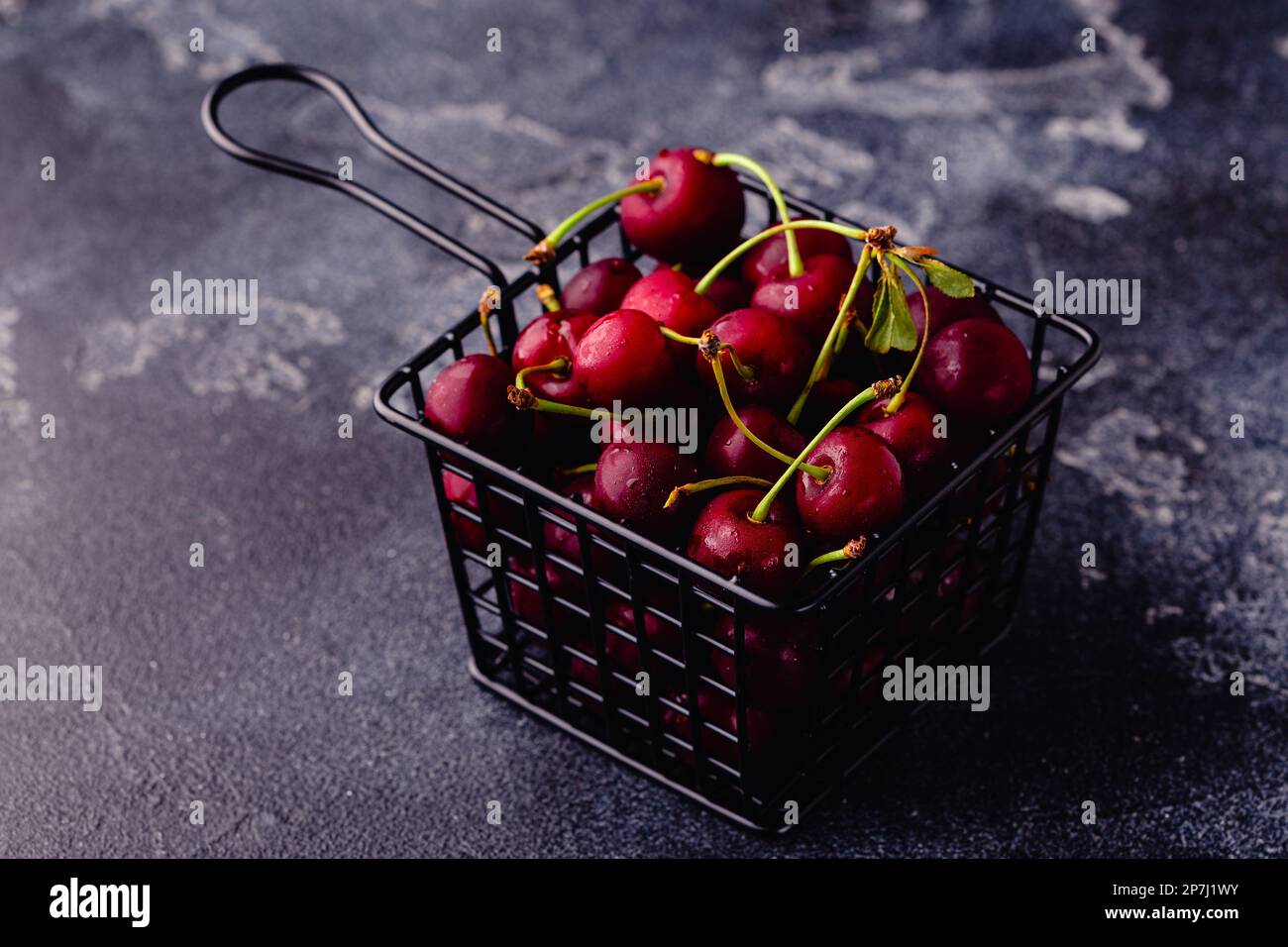 Cerises douces fraîches dans le panier sur fond sombre, mise au point sélective Banque D'Images