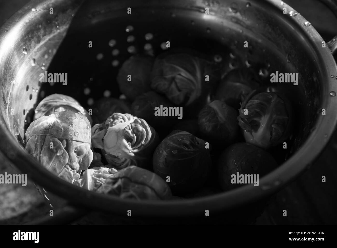 Bruxellois vert non cuit frais et propre dans une vieille passoire en métal avec des gouttes d'eau. Mise au point sélective. Cuisine de style de vie candiée. Noir blanc Banque D'Images