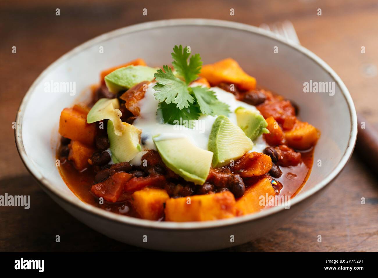 Bol avec un piment à base de patate douce végétalienne de haricots noirs maison avec yaourt au soja et morceaux d'avocat. Banque D'Images