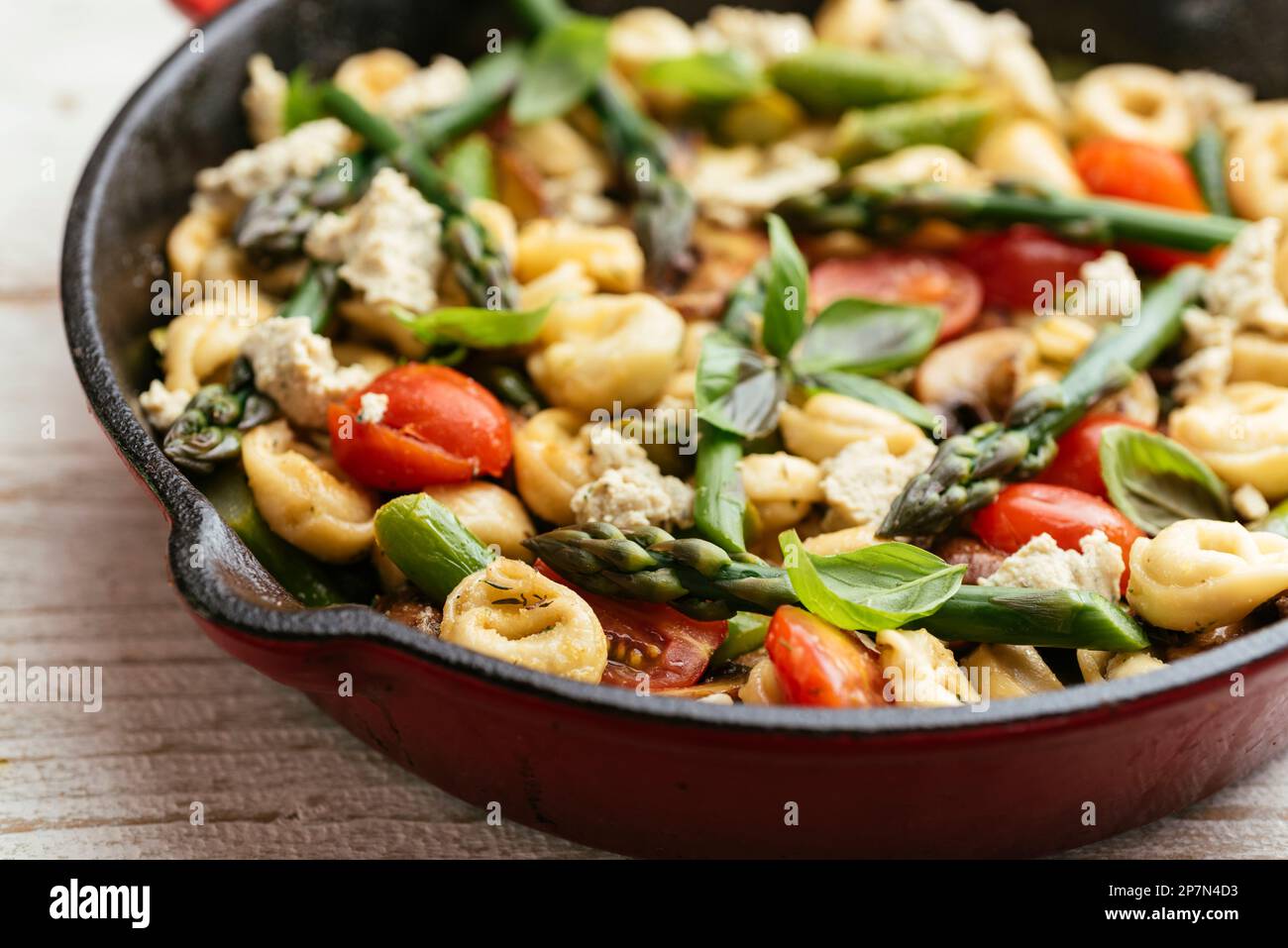 Moule en fonte avec tortellini aux légumes, asperges, tomates, champignons et feta végétalien maison. Banque D'Images