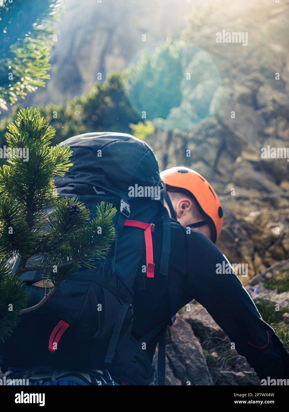 Jeune alpiniste de l'arrière avec un sac à dos et un casque de l'arrière sur un vêtement noir de montagne orange Banque D'Images
