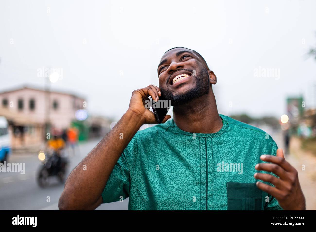 Un jeune Africain enthousiaste qui parle sur un smartphone en plein air, parle avec sa famille à l'étranger. Banque D'Images