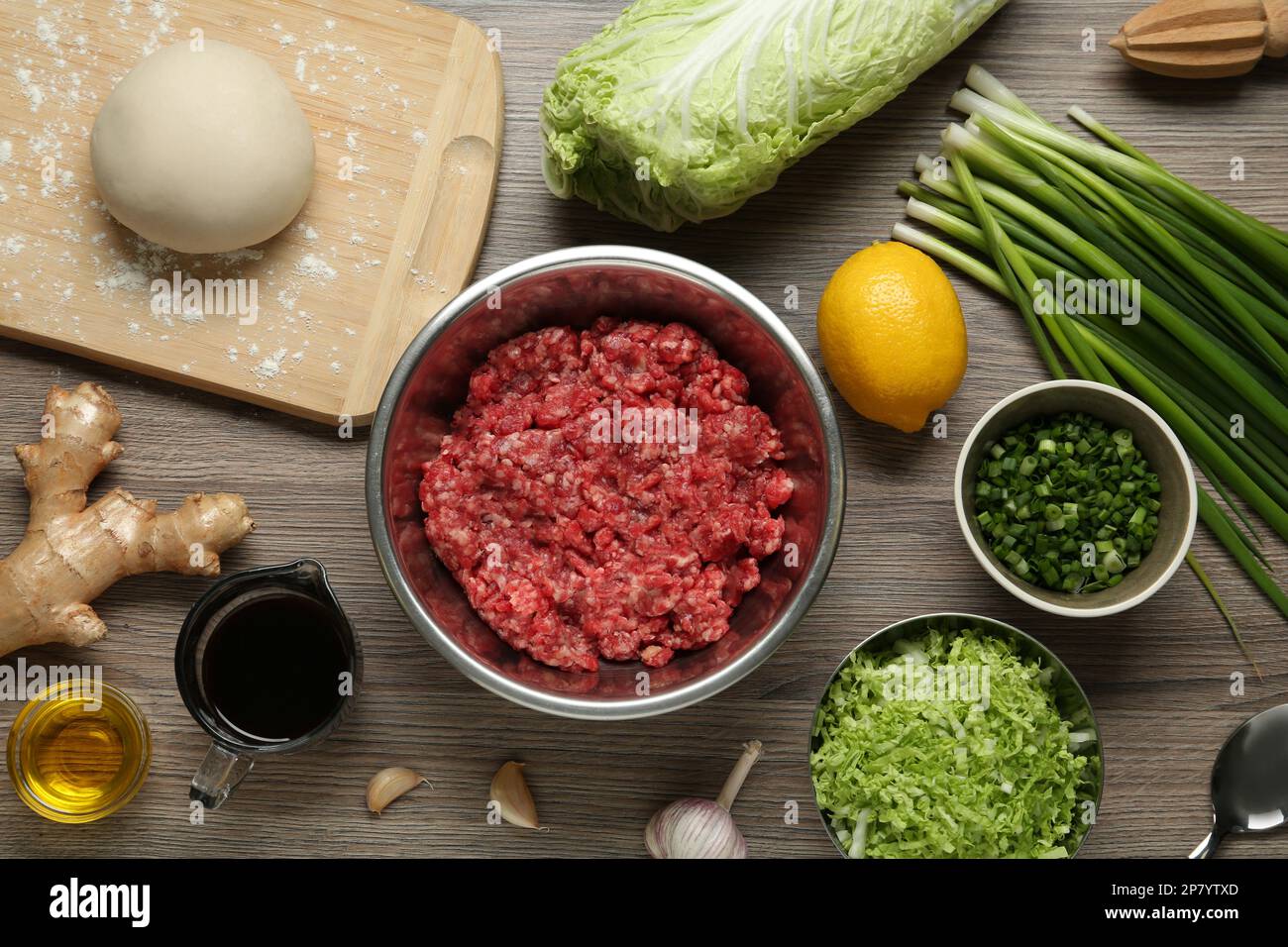 Bol avec viande hachée, pâte crue et ingrédients pour le remplissage de gyoza sur une table en bois, plat Banque D'Images