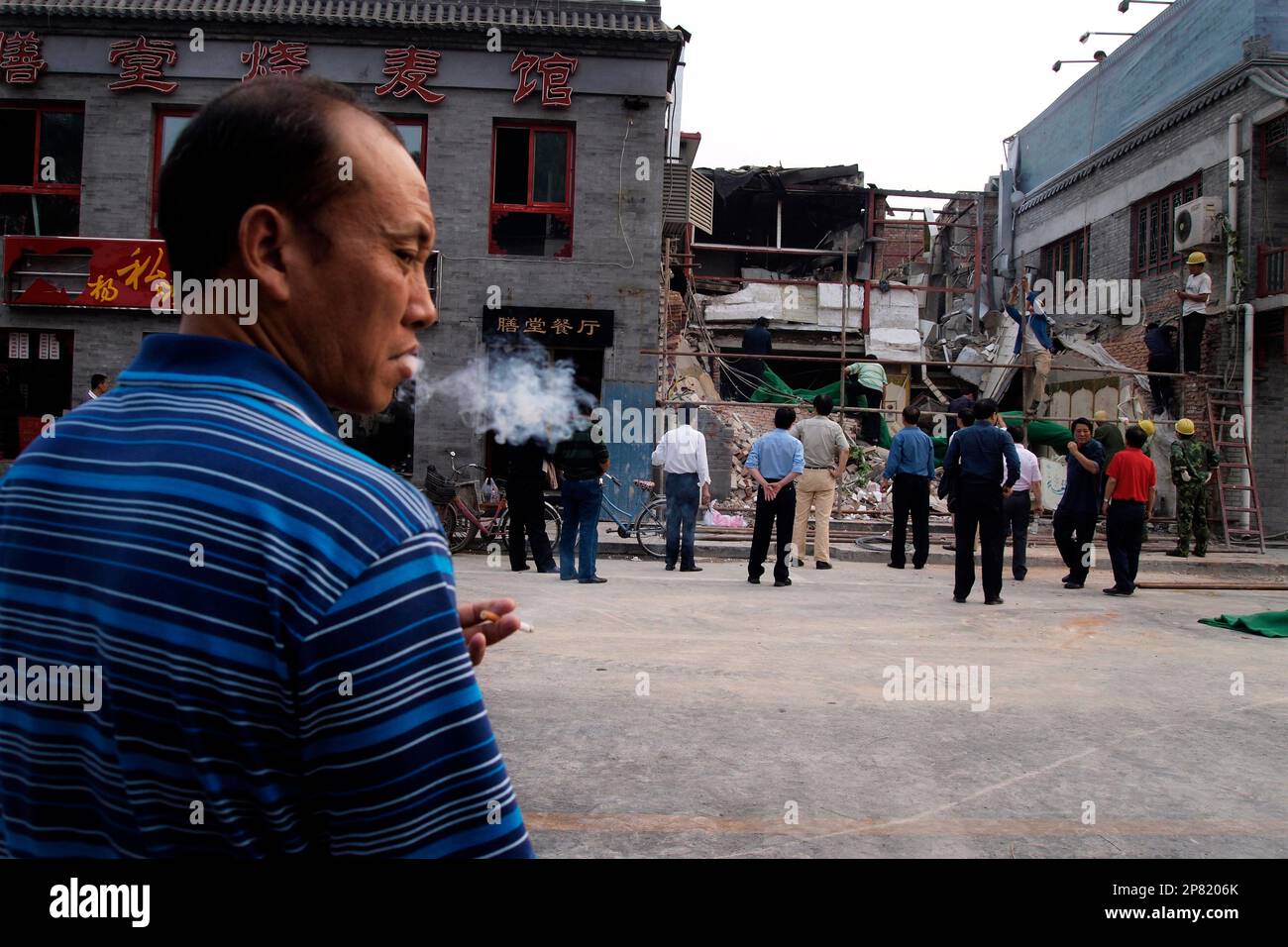 A Chinese man smokes while workers prepare to cover up the remains of an ethnic restaurant in Beijing China, Friday, Sept. 25, 2009. A gas explosion leveled the ethnic restaurant in downtown Beijing early Friday, raising security concerns ahead of China's 60th anniversary celebrations next week. (AP Photo/Ng Han Guan) Banque D'Images