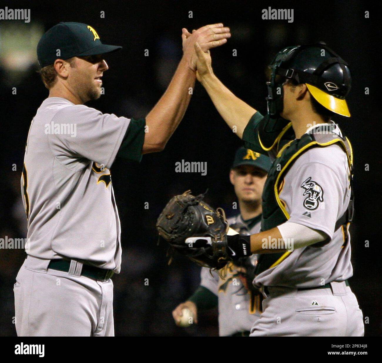 Oakland Athletics starting pitcher Brett Tomko, left, receives a high-five from catcher Kurt Suzuki, right, as Adam Kennedy, rear, looks on following the final out against the Texas Rangers in a baseball game in Arlington, Texas, Monday, Sept. 14, 2009. Tomko pitched a five-hitter for his 100th major league win, as Oakland won 9-0. (AP Photo/Tony Gutierrez) Banque D'Images