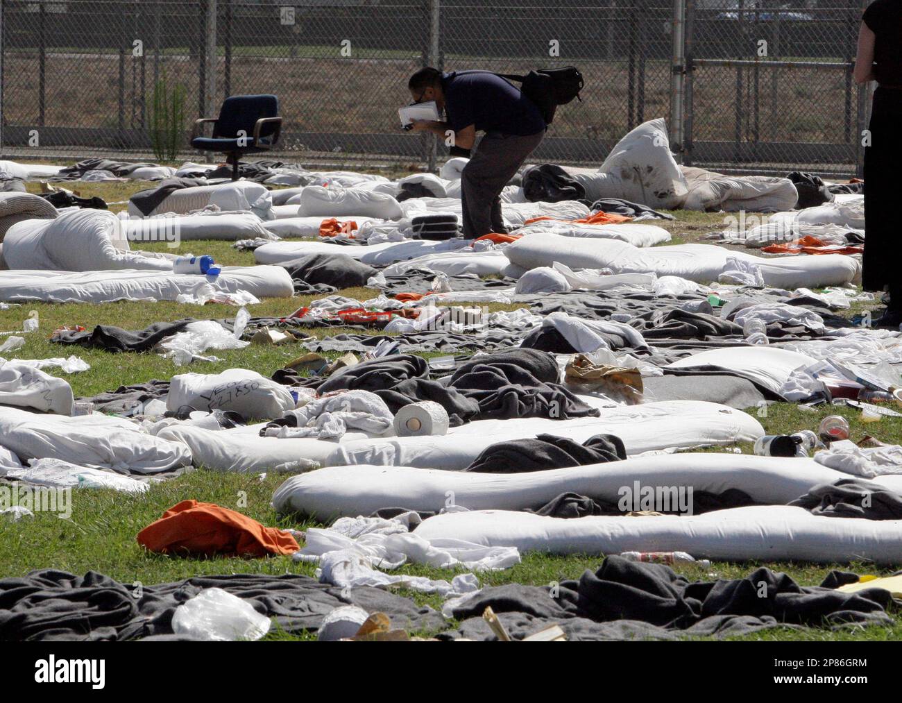 A journalist photographs dozens of mattresses and other debris littering a yard outside a dormitory during a tour of the California Institution for Men in Chino, Calif., Tuesday, Aug. 11, 2009. Blood-soaked mattresses, singed bedding and abandoned backboards and medical supplies littered the campus of the Chino prison Tuesday, a testament to the violence of a weekend riot that shut down part of the institution and injured nearly 200 inmates. (AP Photo/Reed Saxon) Banque D'Images
