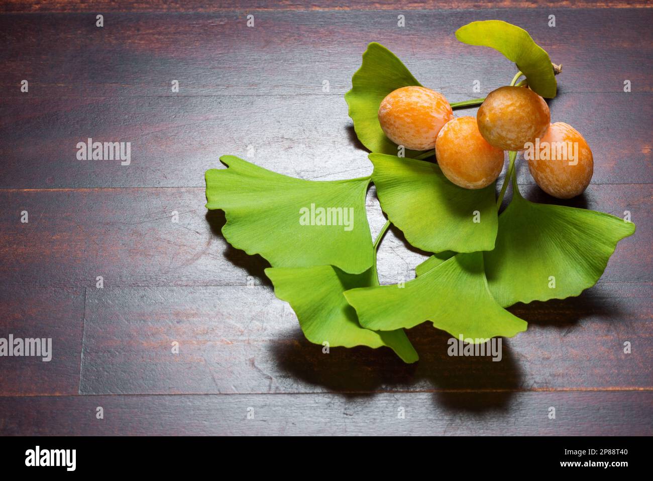 Ginkgo biloba, fruits jaunes mûrs et feuilles vertes sur fond de bois. Banque D'Images