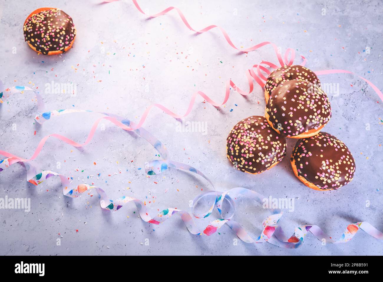 Pâtisserie berlinère au chocolat pour le carnaval et la fête. Krapfen allemand ou beignets avec des banderoles et des confettis. Image de carnaval ou d'anniversaire colorée Banque D'Images