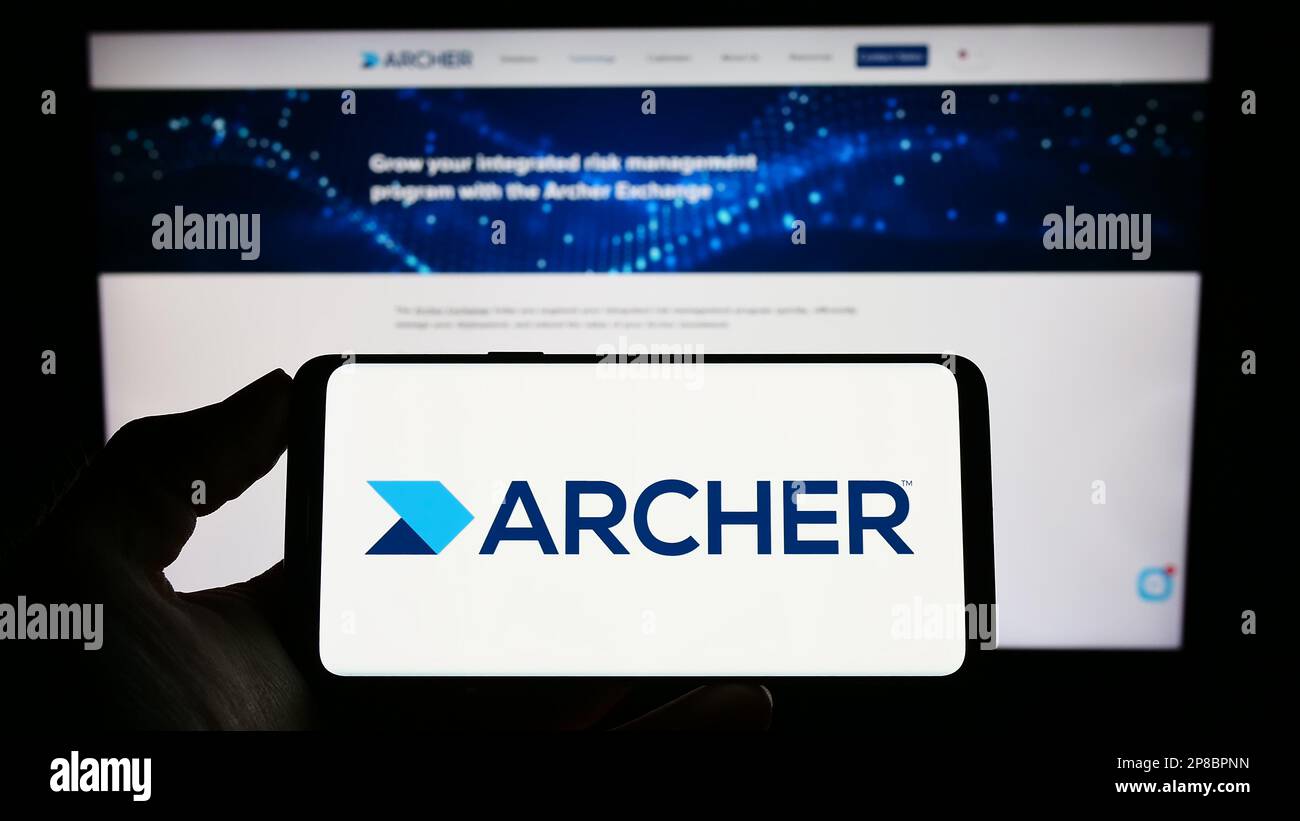 Personne tenant un téléphone portable portant le logo du logiciel de gestion des risques Archer (RSA Security) à l'écran devant la page Web. Mise au point sur l'affichage du téléphone. Banque D'Images