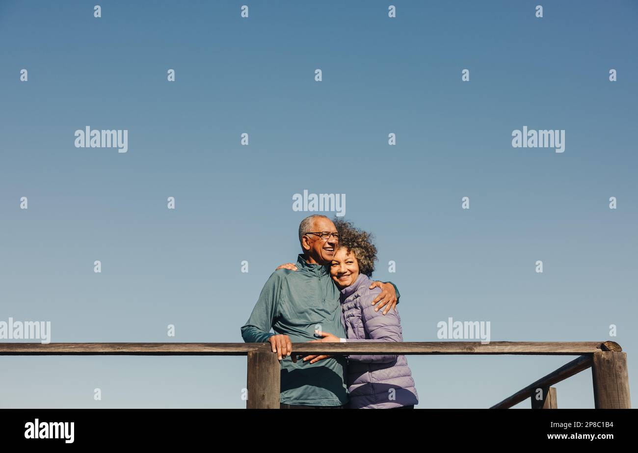 Couple romantique de personnes âgées souriant et s'embrassant tout en se tenant sur un pont de pied en bois. Couple senior heureux appréciant un séjour en bord de mer reposant Banque D'Images