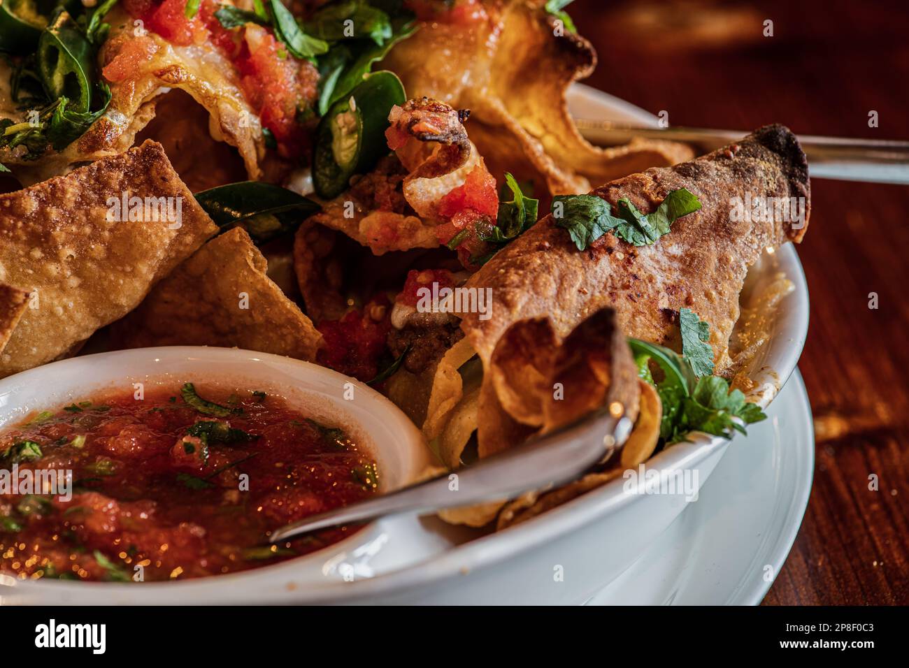 Gros plan d'une assiette de chips avec de la viande, du fromage fondu, des herbes, du piment vert et de la sauce à la sauce tomate Banque D'Images