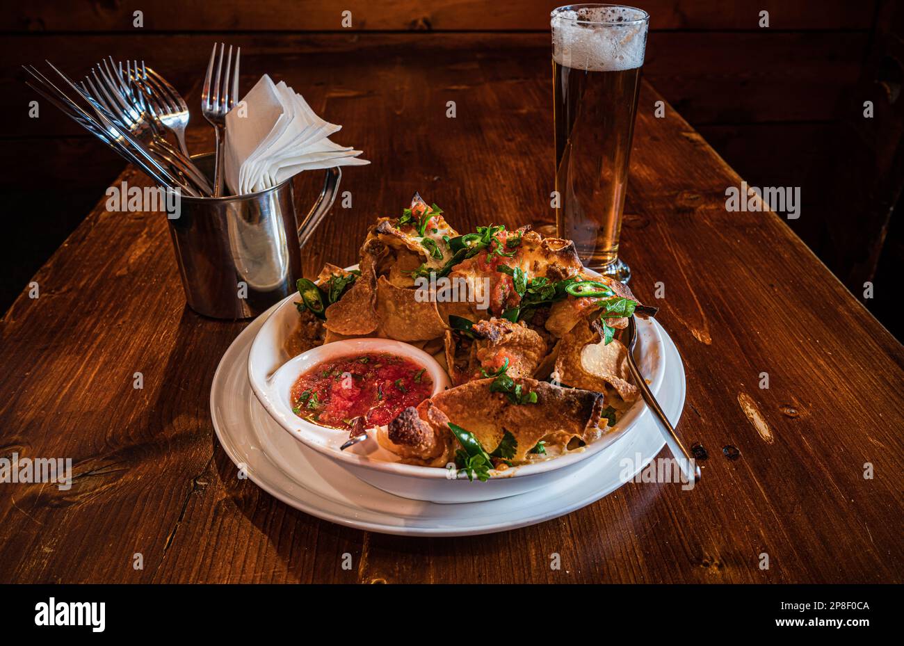 Gros plan d'une assiette de chips avec de la viande, du fromage fondu, des herbes, du piment vert, de la sauce à la sauce tomate et un verre de bière Banque D'Images