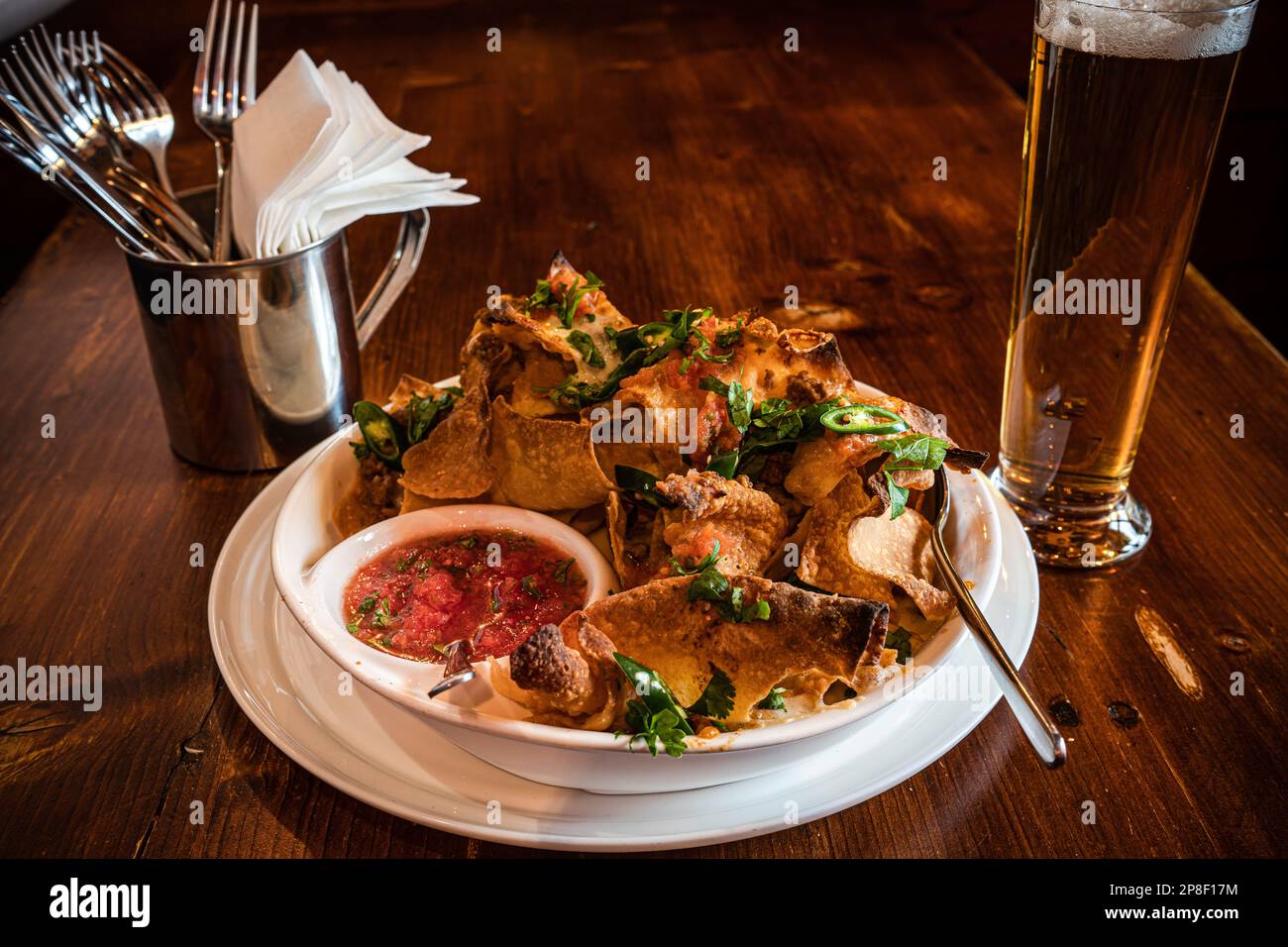Gros plan d'une assiette de chips avec de la viande, du fromage fondu, des herbes, du piment vert, de la sauce à la sauce tomate et un verre de bière Banque D'Images