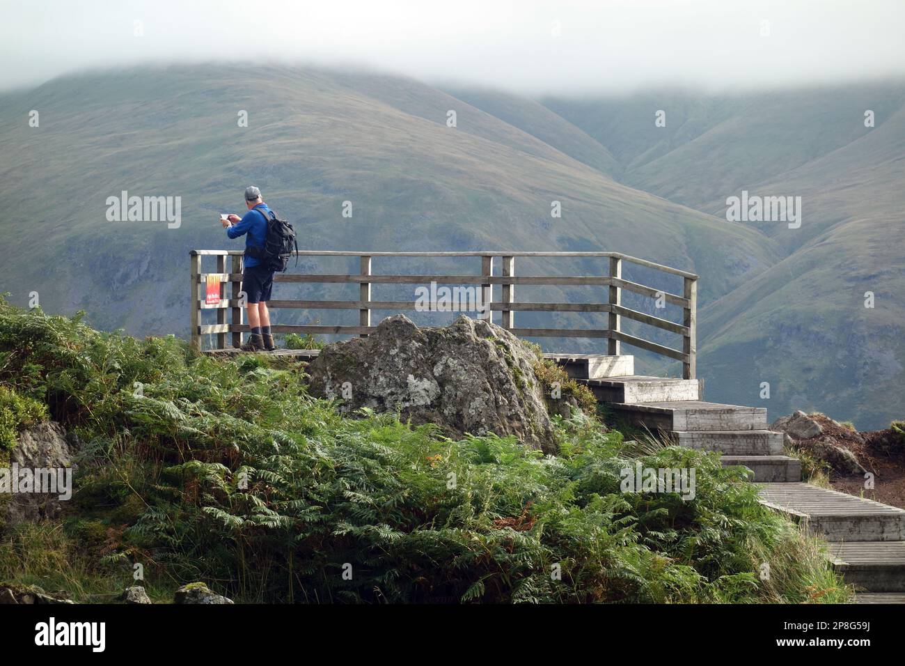 Homme prenant des photos sur la plate-forme d'observation en bois sur le Wainwright 'Raven Crag' Thirlmere dans le parc national de Lake District, Cumbria, Angleterre, Royaume-Uni. Banque D'Images