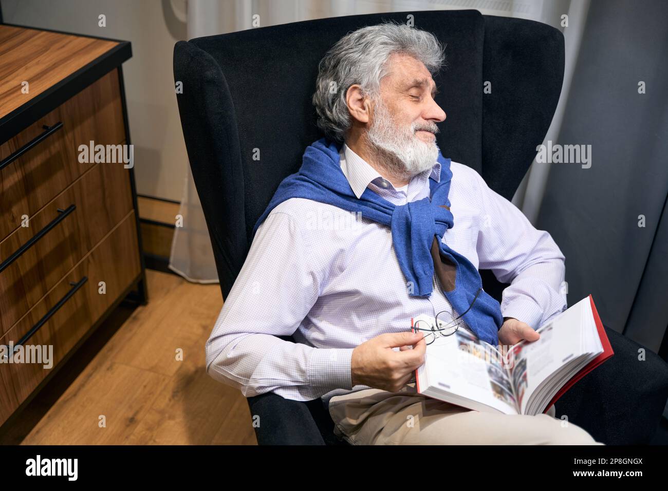 Agréable homme âgé qui se délassant dans une chaise confortable Banque D'Images