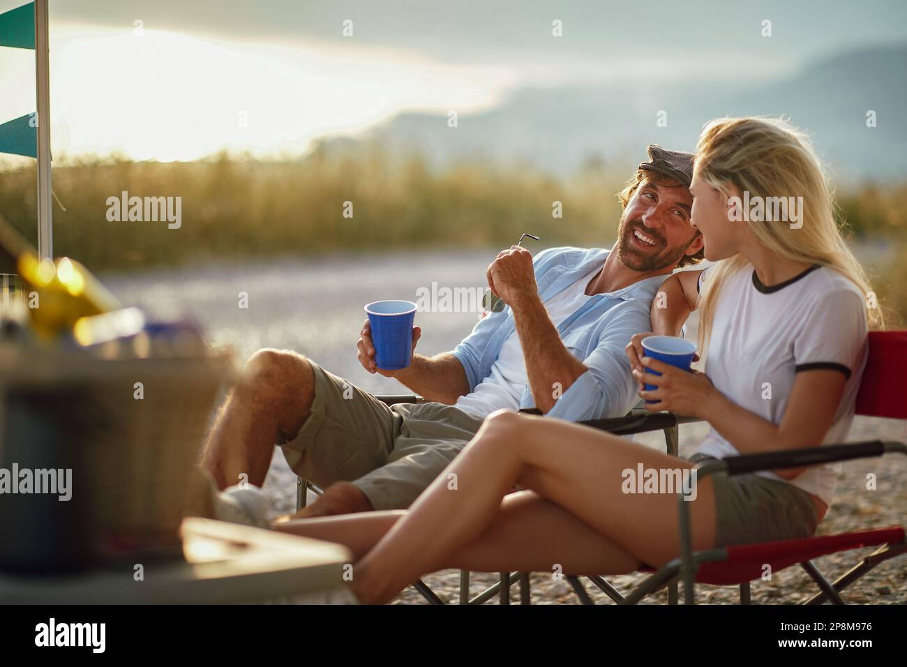 couple d'adultes caucasiens parlant et souriant, regardant l'un l'autre, assis à l'extérieur au coucher du soleil Banque D'Images