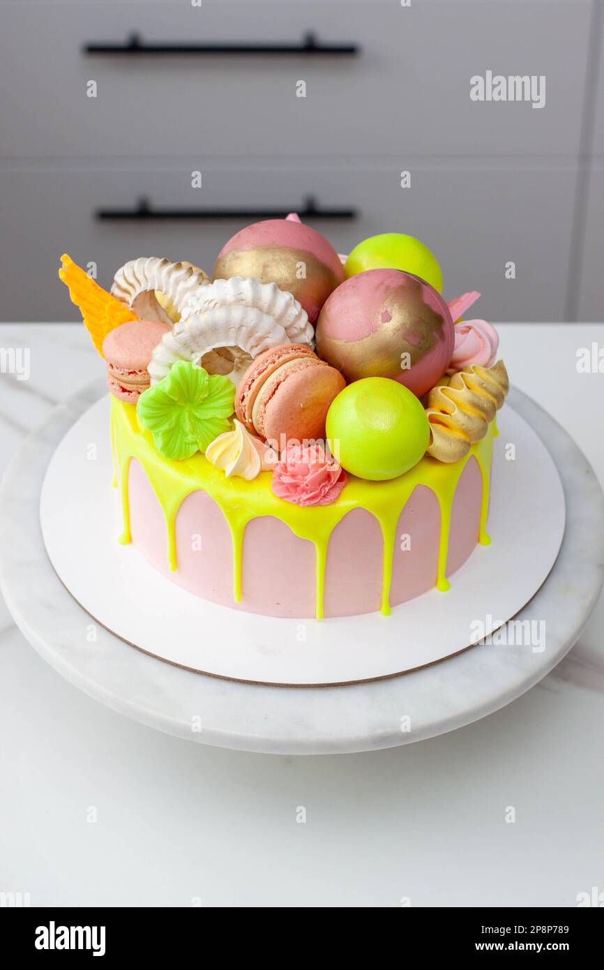 Gâteau d'anniversaire vert néons, citron vert et rose au goutte d'eau heureux surmonté d'un assortiment de fleurs en chocolat de couleur arc-en-ciel, de boules, de meringues et de bonbons Banque D'Images