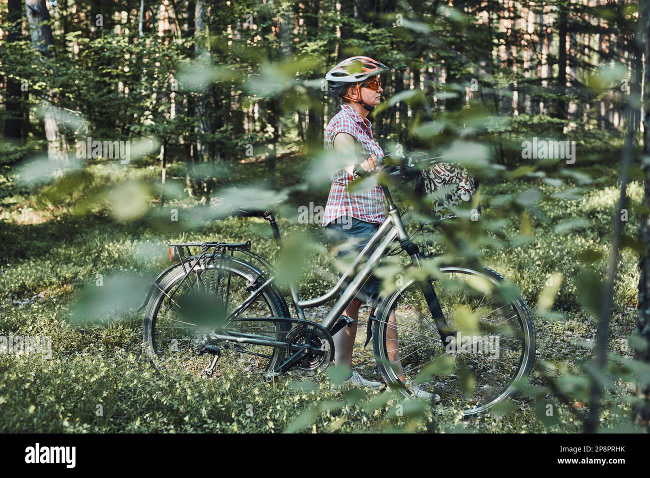 Femme active qui passe du temps libre lors d'une excursion à vélo dans une forêt le jour d'été ensoleillé. Femme portant un casque de vélo et des gants tenant le vélo avec Banque D'Images