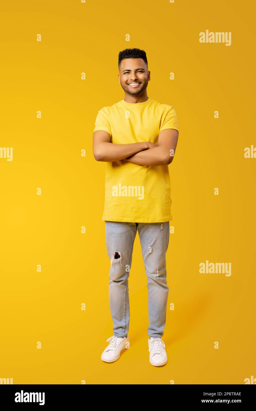Portrait pleine longueur du jeune Indien confiant et heureux 20s en t-shirt jaune tenant les mains croisées isolé sur fond jaune Uni, étudiant étranger Banque D'Images