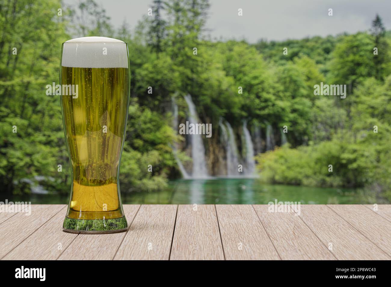 Verre de bière légère sur la table avec vue sur la forêt avec lac et cascade Banque D'Images
