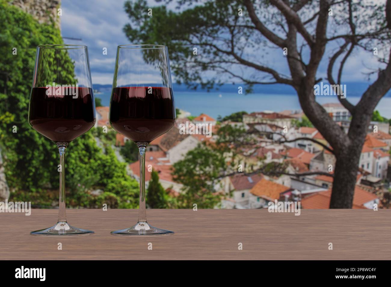 Deux verres de vin rouge avec vue sur la ville croate d'omis avec des toits rouges et la mer bleue. Banque D'Images