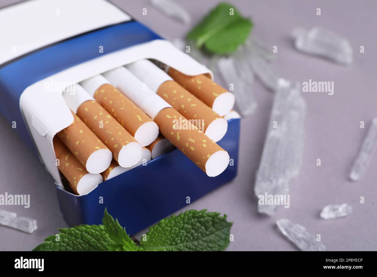Paquet de cigarettes, de cristaux de menthol et de feuilles de menthe sur fond gris, gros plan Banque D'Images