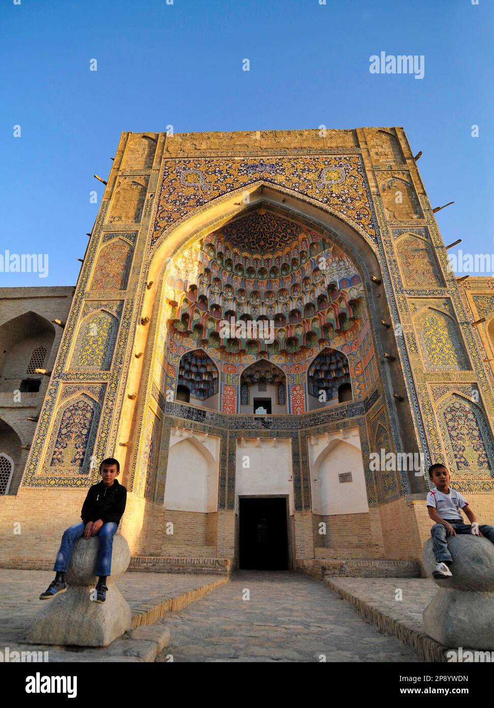 Des enfants ouzbèkes assis devant la Madrassah Abdulaziz Khan dans la vieille ville de Boukhara, en Ouzbékistan. Banque D'Images