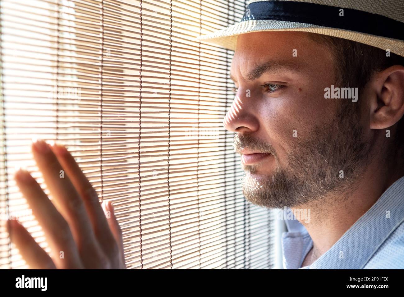 Homme dans chapeau de paille regardant par la fenêtre à travers les stores de paille. Banque D'Images