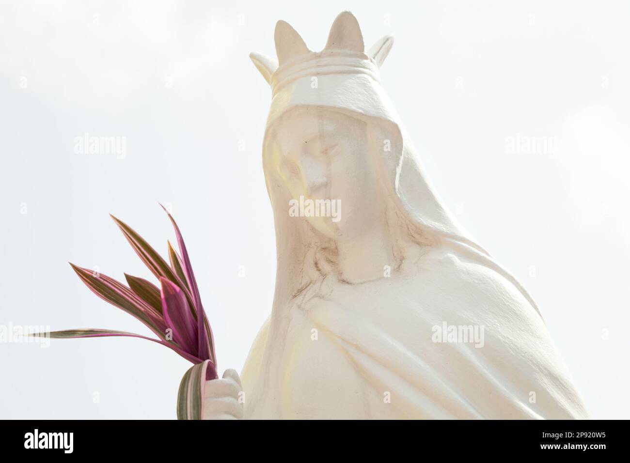 Ancienne sculpture d'un blanc saint femme portant une couronne et tenant un bouquet. Sainte catholique statue vintage contre la lumière ciel Banque D'Images