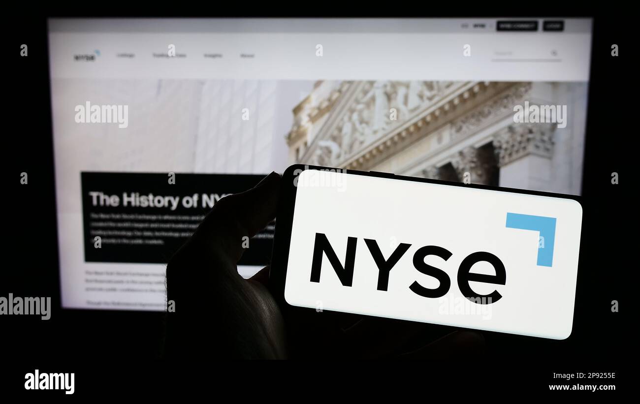 Personne tenant un téléphone portable avec le logo du marché américain de la Bourse de New York (NYSE) à l'écran en face de la page web. Mise au point sur l'affichage du téléphone. Banque D'Images