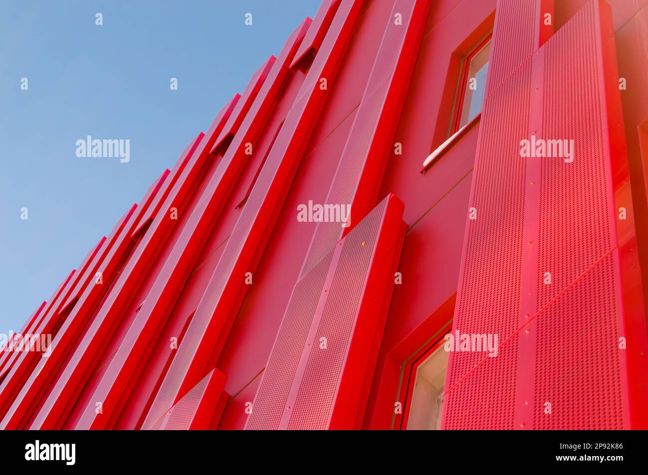 Bâtiment moderne de bureau architectural rouge. Tôles recouvrant l'extérieur de la structure. Bâtiment unique de style futuriste. Ciel dégagé à l'arrière Banque D'Images