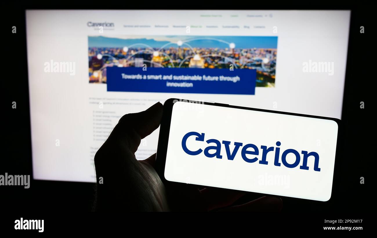 Personne tenant le téléphone cellulaire avec le logo de la société de technologie du bâtiment Caverion Oyj à l'écran en face de la page Web d'affaires. Mise au point sur l'affichage du téléphone. Banque D'Images