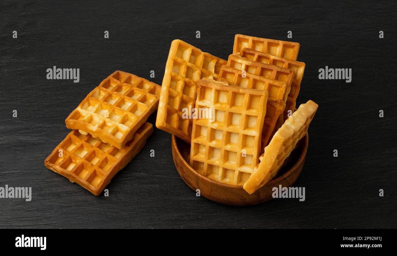 Belge Waffle Isolated, cuisine gaufrée carrée dans un bol en bois, gaufres belges dorées maison, petit déjeuner Wafer Biscuit sur fond noir Banque D'Images